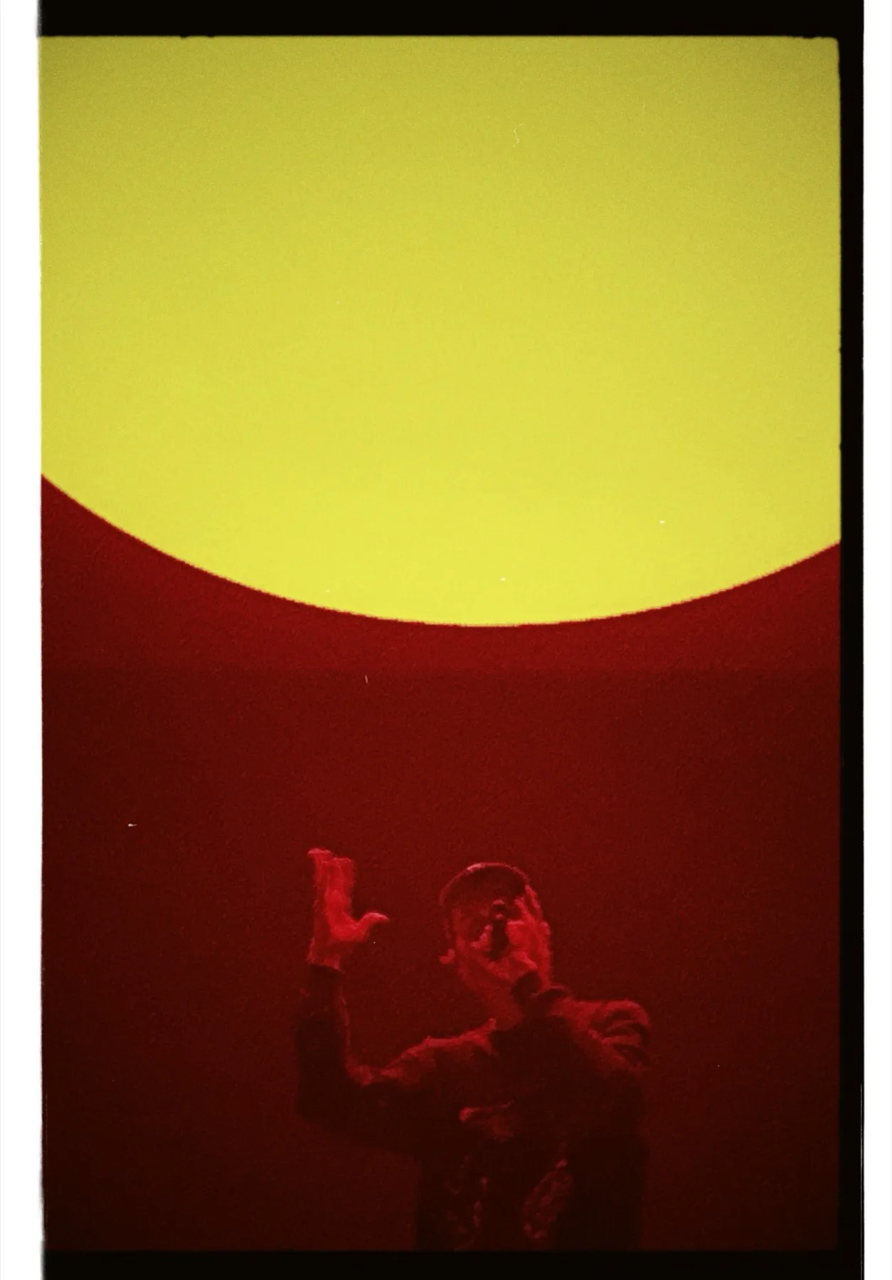 Silhouette a braccia alzate sotto una proiezione LED circolare rossa e gialla, cornice pellicola