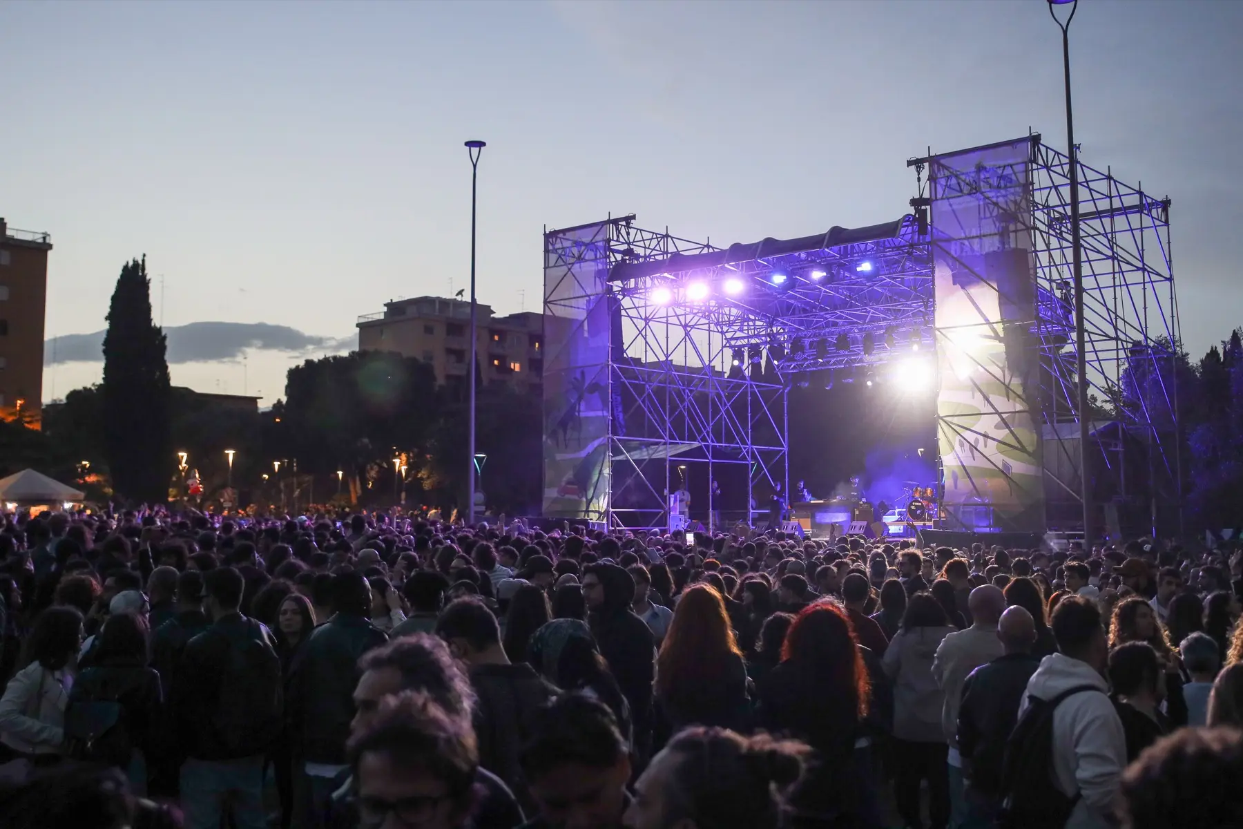Il palco illuminato di blu al calare della sera, pubblico in controluce