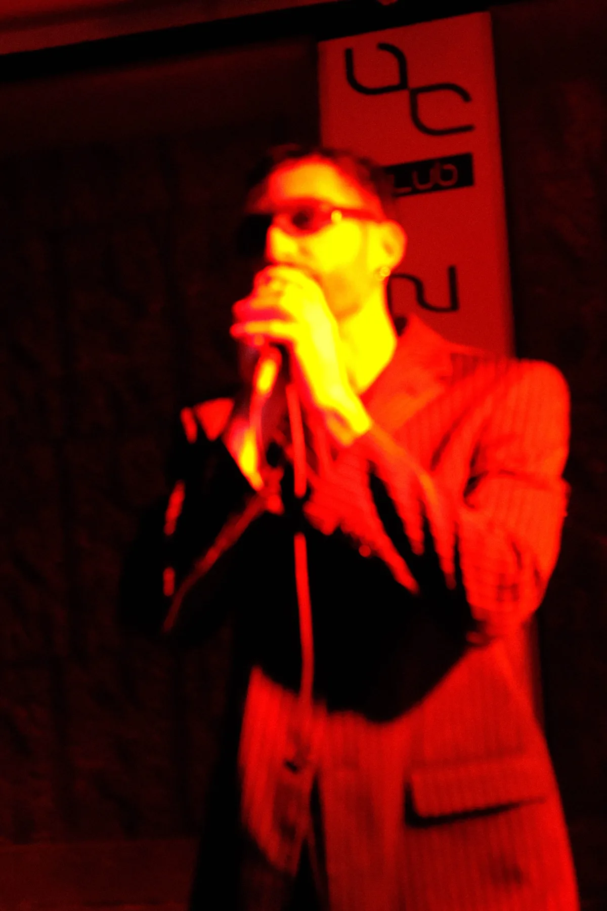 Cantante con occhiali da sole in controluce rosso, microfono in mano